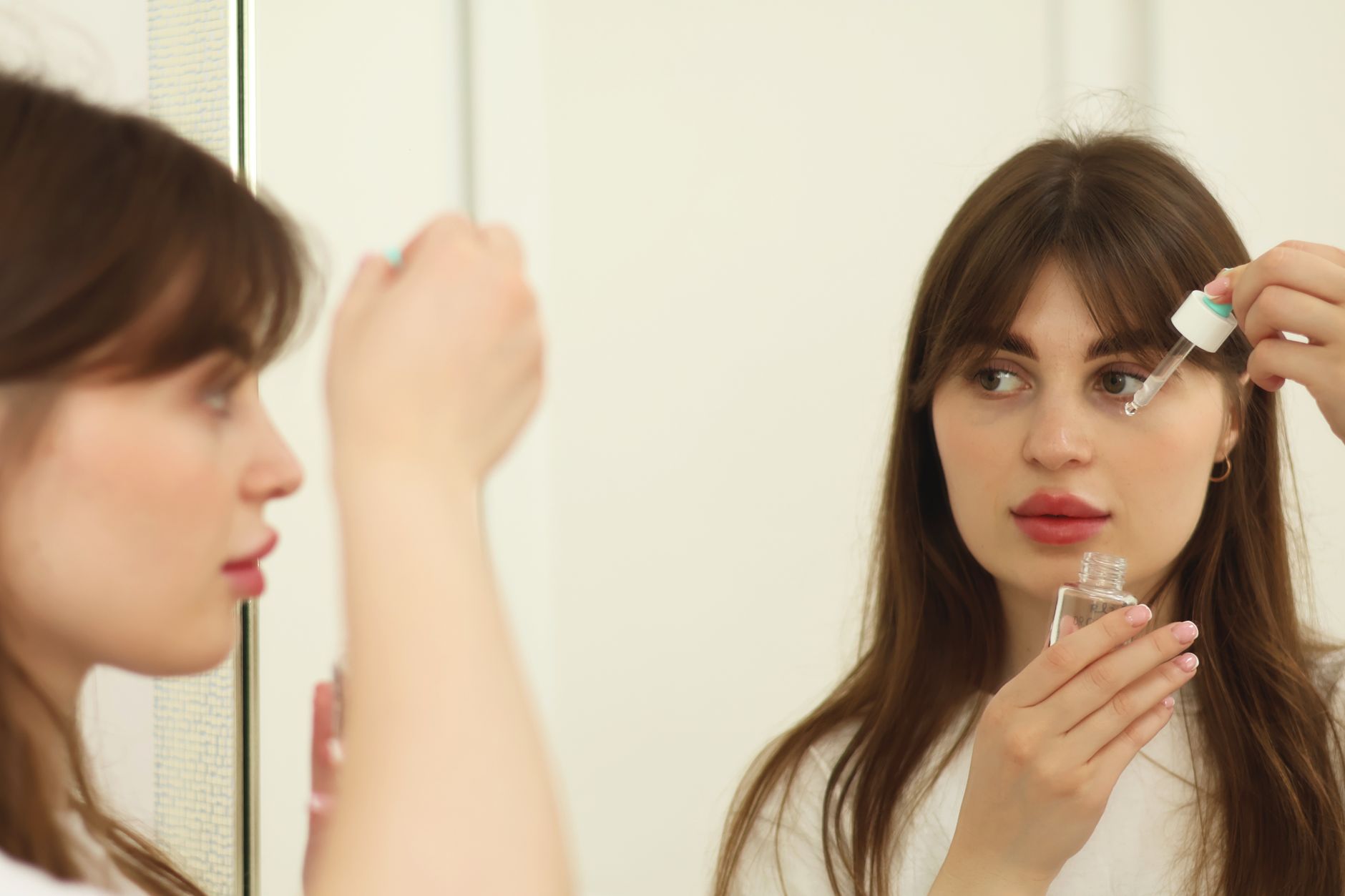A person gently applying skincare product to their face in a well-lit bathroom