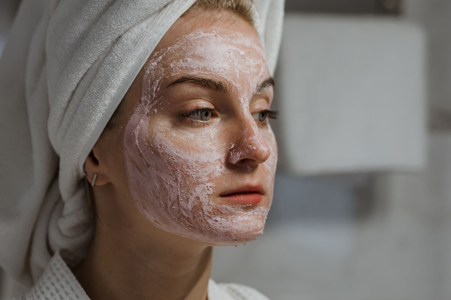 Close-up of a person's face with a glowing forehead, suggesting oily skin, with a lightweight ceramide moisturizer bottle blurred in the background.